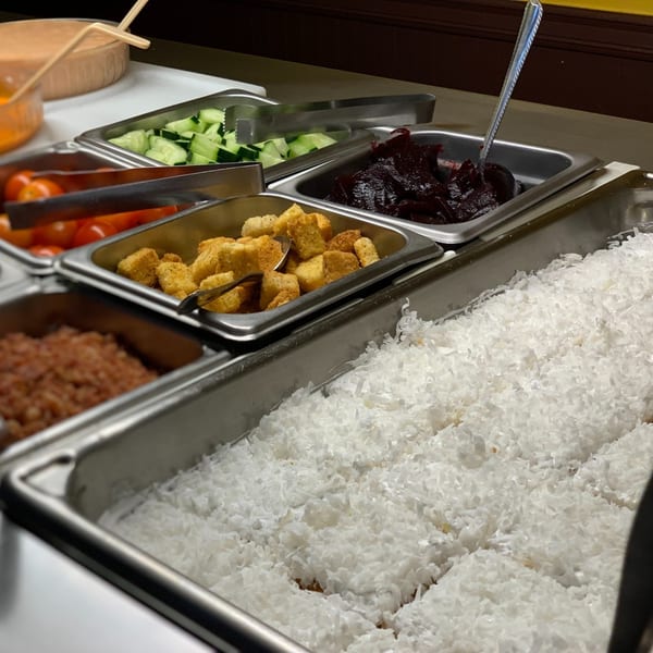 A buffet line with various Mexican food items including rice, beans, and toppings in metal trays.