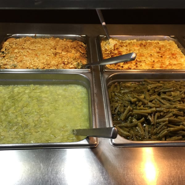 A buffet line with four trays of food: a casserole, mac and cheese, lima beans, and green beans.
