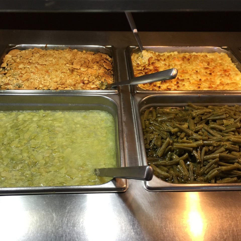 A buffet line with four trays of food: a casserole, mac and cheese, lima beans, and green beans.