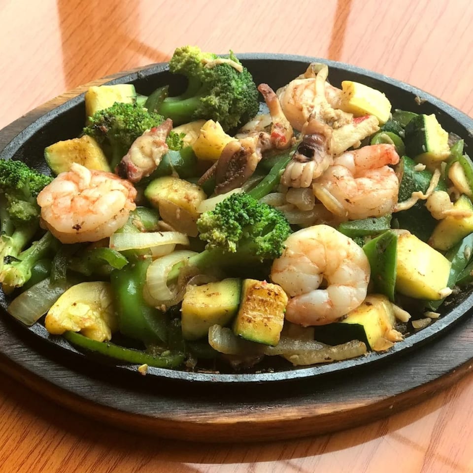 Sizzling shrimp fajitas with broccoli, zucchini, and bell peppers on a cast iron plate.