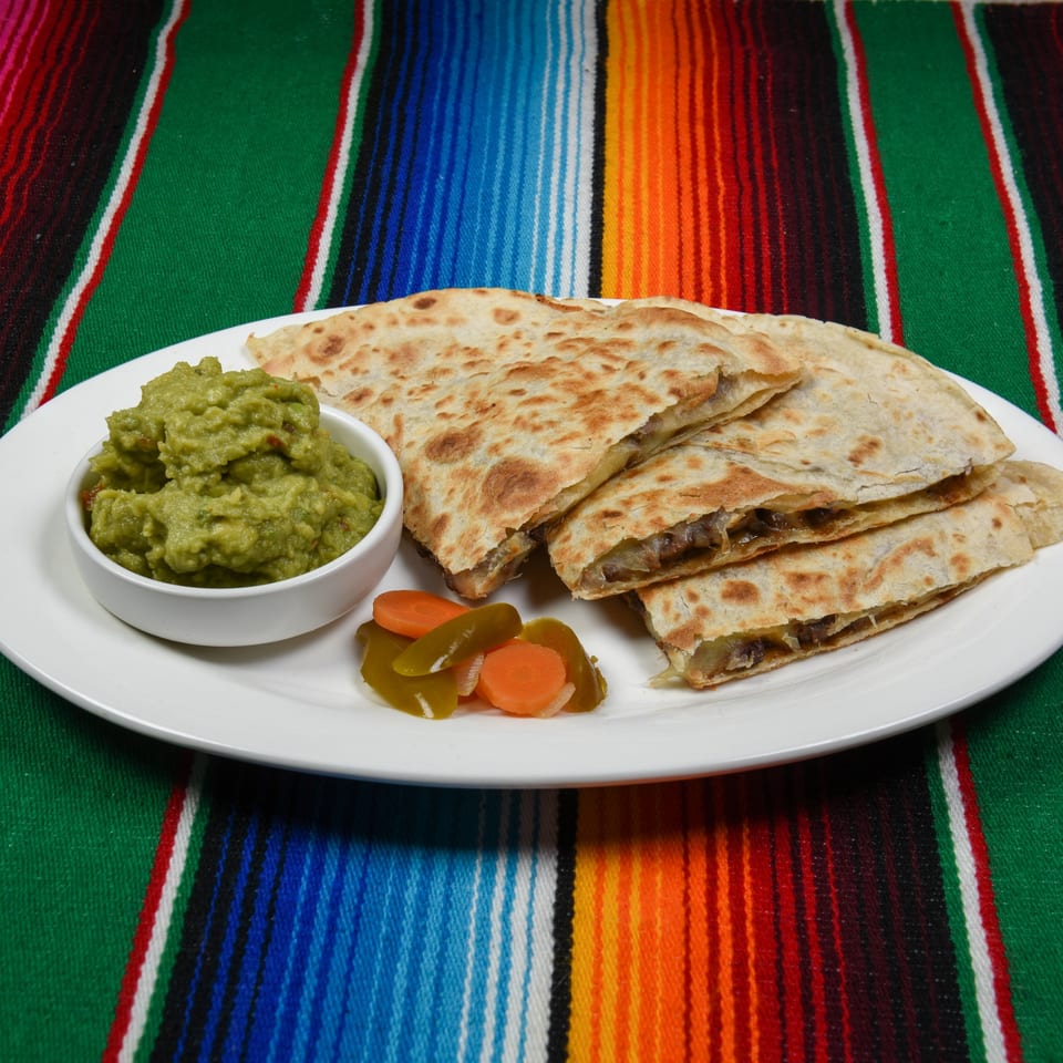 Quesadillas with guacamole and pickled vegetables on a white plate, set on a colorful striped Mexican blanket.