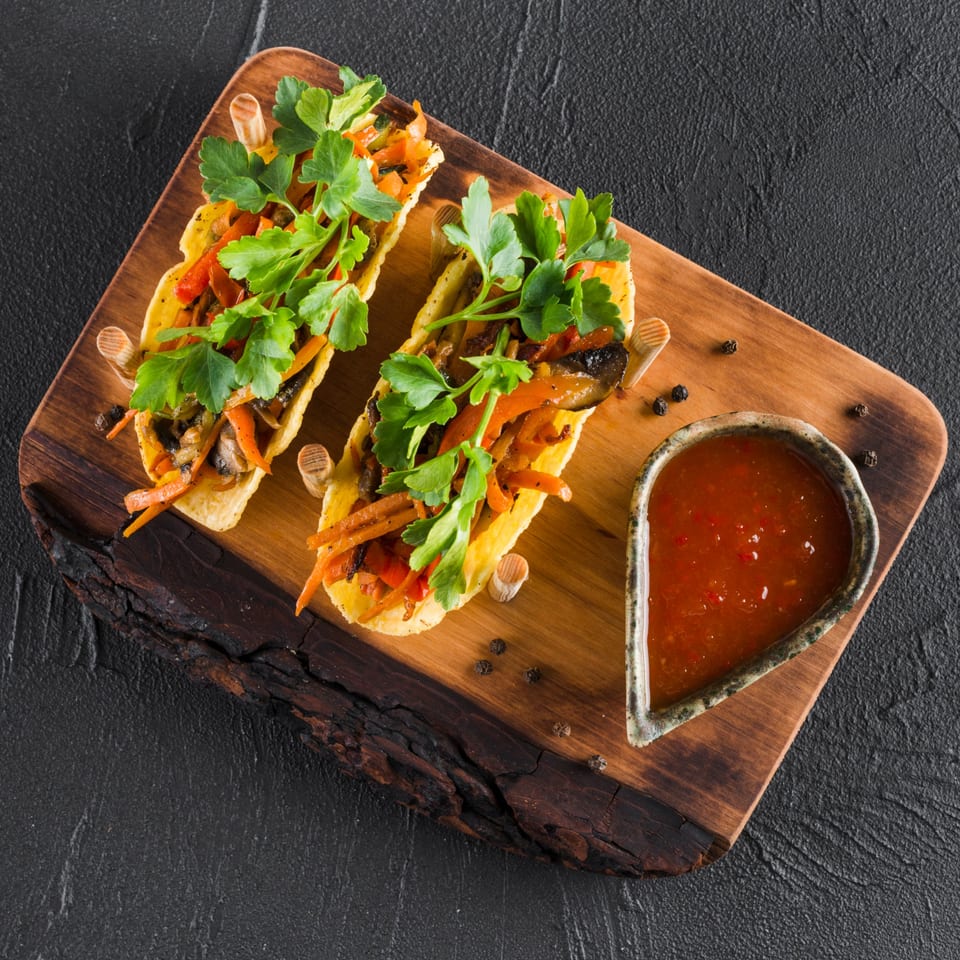 Two vibrant Casa Grande Cantina & Grill tacos filled with vegetables and fresh parsley, served with salsa.