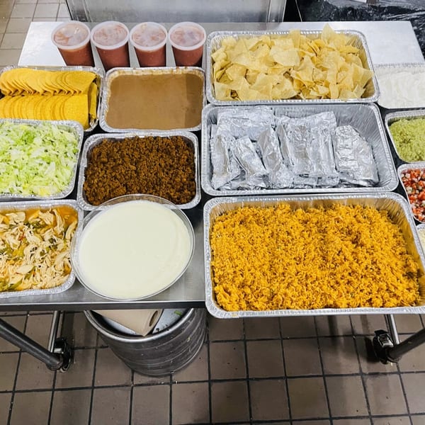 A catering spread of Mexican food including tacos, rice, beans, salsa, and guacamole.