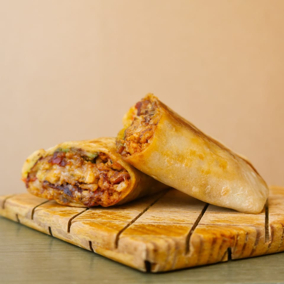 Two golden-brown burritos, one cut open to reveal a savory filling, on a wooden board.